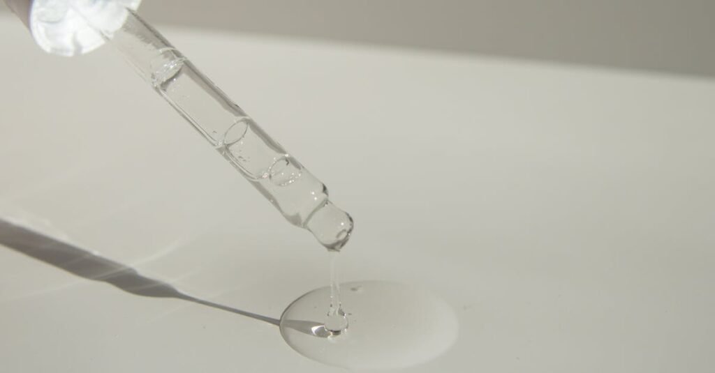 Close-up of a cosmetic pipette releasing serum onto a surface with soft sunlight.